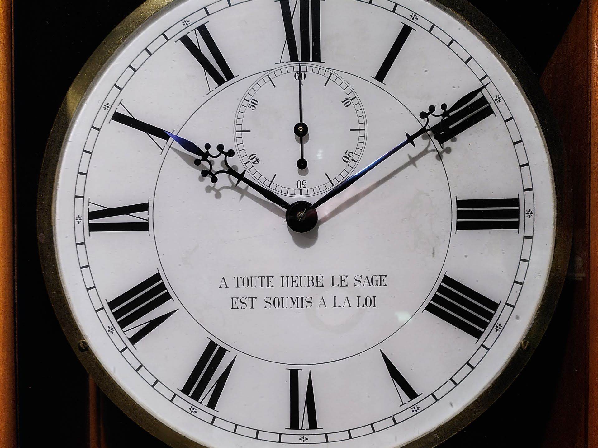 A clock face with an inscription in French: "à toute heure le sage est soumis à la loi"